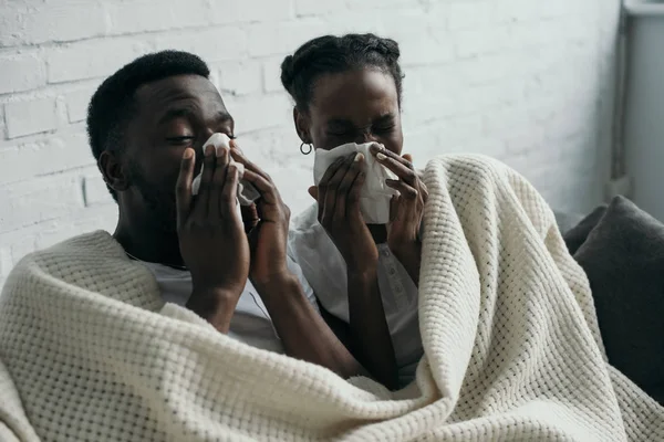 Jeune couple afro-américain tenant des serviettes en papier tout en ayant la grippe ensemble à la maison — Photo de stock