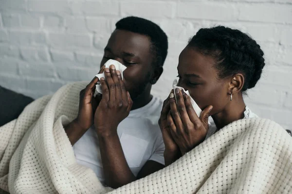 Junges krankes Paar hält Papierservietten in der Hand und liegt zu Hause unter Decke zusammen — Stockfoto