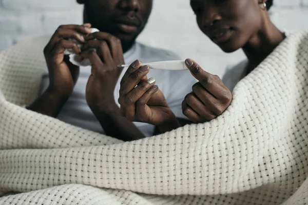 Cropped shot of young african american couple checking thermometer while having flu together — Stock Photo