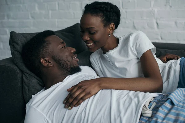 Beautiful happy young african american couple in pajamas smiling each other at home — Stock Photo