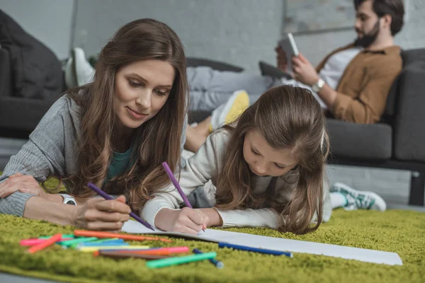 Mãe e filha desenho no chão, enquanto o pai usando tablet no sofá na sala de estar — Fotografia de Stock