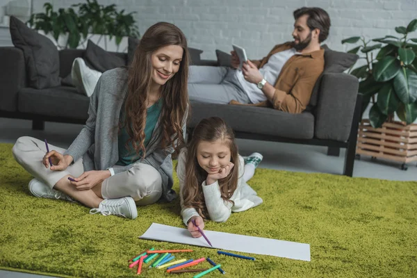 Mutter und Tochter zeichnen auf dem Boden und Vater mit Tablet auf dem Sofa — Stockfoto