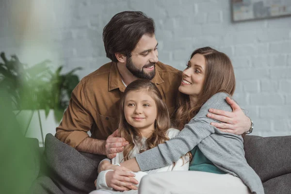 Счастливые родители и дочь обнимаются на диване — стоковое фото