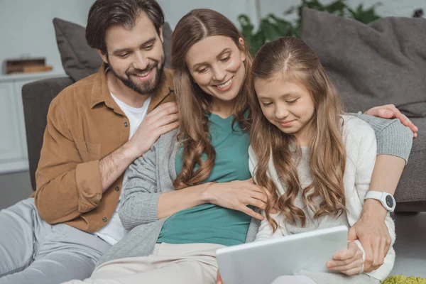 Padres felices y la hija usando el ordenador portátil en la sala de estar - foto de stock