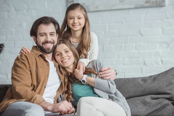 Sonrientes padres e hija mirando a la cámara en la sala de estar - foto de stock