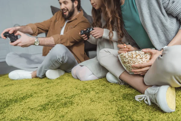 Immagine ritagliata di genitori e figlia che giocano al videogioco e mangiano popcorn — Foto stock