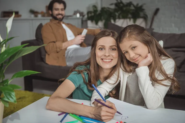 Mother helping daughter drawing with felt-tip pens and looking at camera — Stock Photo