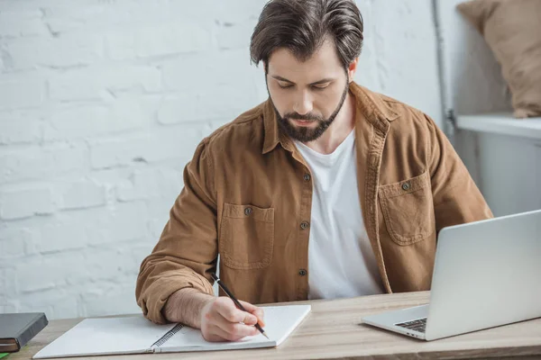 Schöner Geschäftsmann, der im Büro etwas ans Notizbuch schreibt — Stockfoto