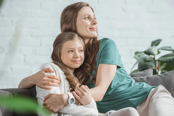 Madre e hija abrazándose y mirando hacia otro lado en casa - foto de stock