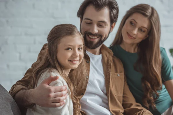 Fille souriante assise avec les parents sur le canapé à la maison — Photo de stock