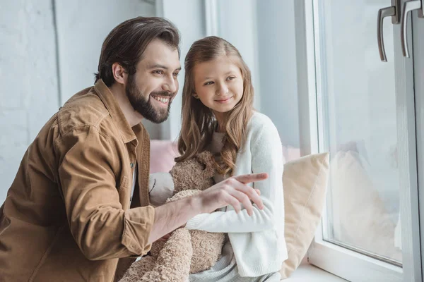 Sonriente padre señalando algo a la hija en la ventana — Stock Photo
