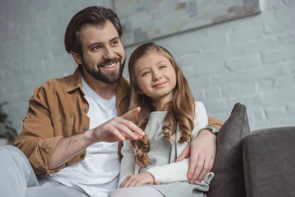 Sonriente padre señalando algo a su hija en casa - foto de stock
