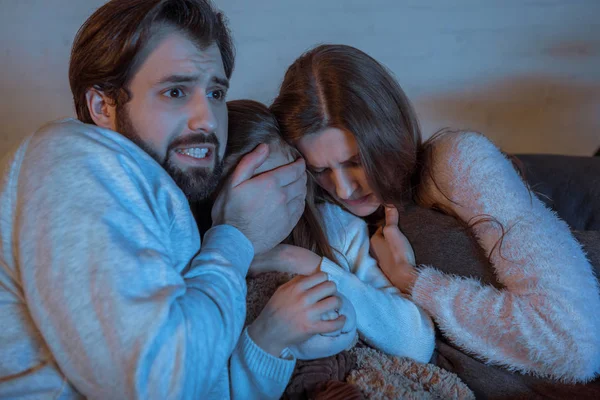 Parents and daughter watching horror movie in evening — Stock Photo