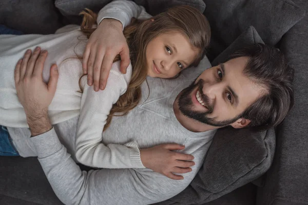 Aus der Vogelperspektive: Vater und Tochter umarmen sich auf dem Sofa und blicken in die Kamera — Stockfoto
