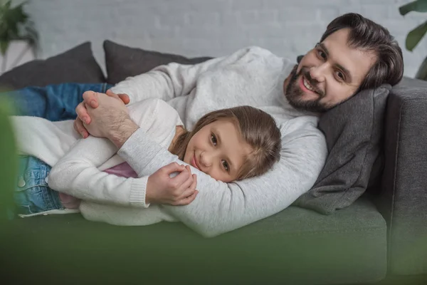 Батько і дочка лежать на дивані і дивляться на камеру — стокове фото