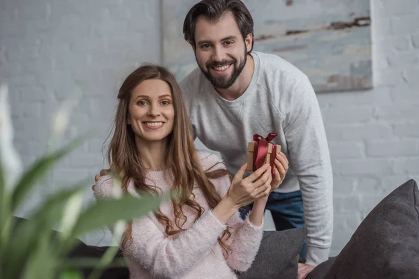 Happy girlfriend holding gift on 8 march and looking at camera at home — Stock Photo
