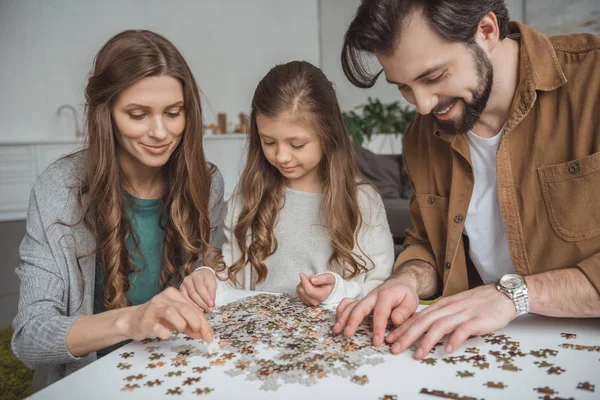 Genitori felici e figlia che collegano pezzi di puzzle a tavola — Foto stock