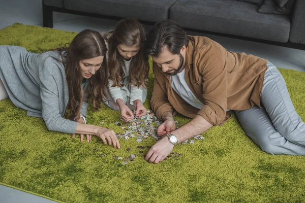Vista ad alto angolo di genitori e figlia che collegano pezzi di puzzle sul tappeto in soggiorno — Foto stock