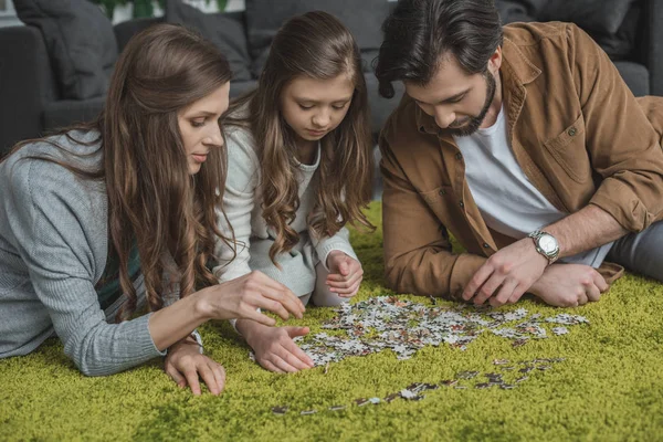 Parents et fille reliant pièces de puzzle sur le sol dans le salon — Photo de stock