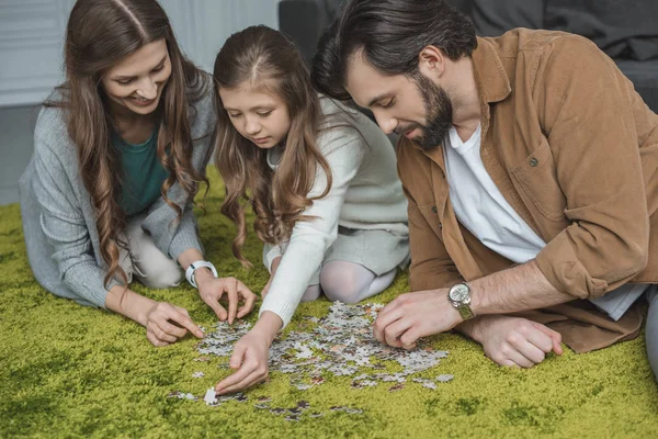 Padres e hija conectando piezas de rompecabezas en la alfombra en la sala de estar - foto de stock