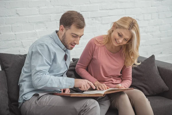 Happy family looking at photos in photo album together at home — Stock Photo