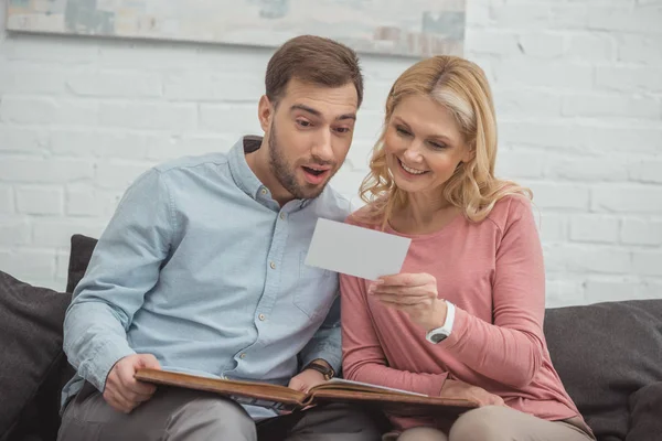 Mutter und erwachsener Sohn betrachten ein Foto in der Hand, während sie gemeinsam auf dem Sofa liegen — Stockfoto