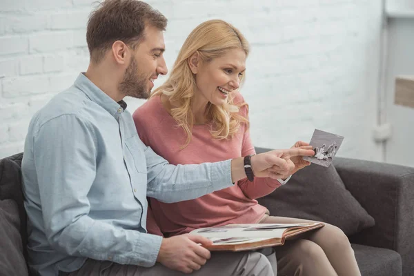 Madre e hijo crecido mirando la foto en la mano mientras descansan juntos en el sofá - foto de stock