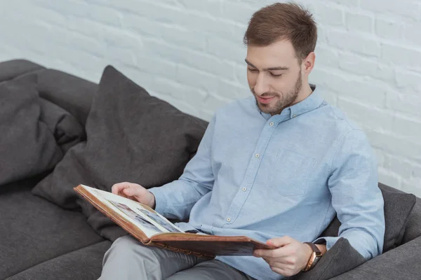 Portrait of man looking at photos in photo album while resting on sofa at home — Stock Photo