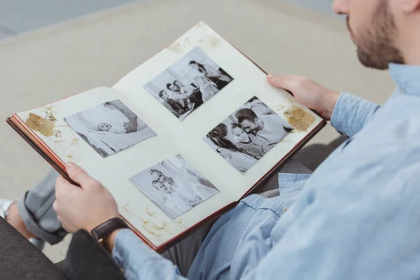 Partial view of man with photo album in hands resting on sofa at home — Stock Photo