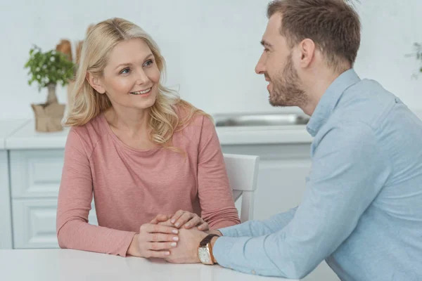 Lächelnde Mutter und erwachsener Sohn halten Händchen, während sie am Tisch sitzen — Stockfoto