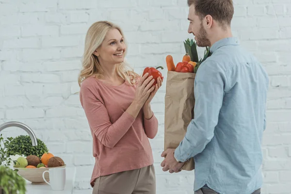 Portrait of grown son and mother with paper bag full of fresh vegetables for dinner at home — Stock Photo