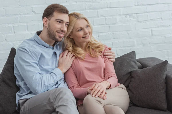 Porträt eines lächelnden Sohnes, der Mutter umarmt, während er zu Hause auf dem Sofa ruht — Stockfoto