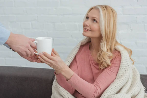 Cultivé fils adulte prudent apporté tasse de thé à la mère dans la couverture sur le canapé à la maison — Photo de stock