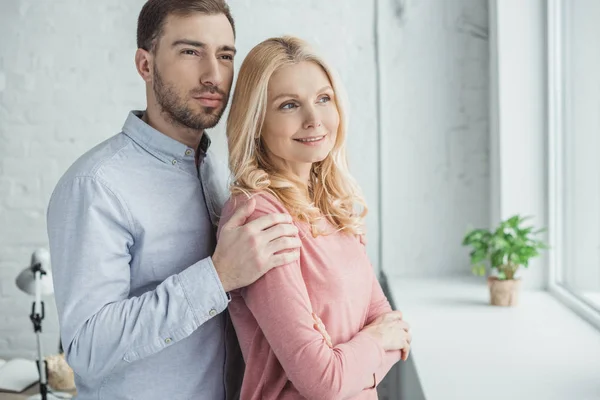 Porträt eines nachdenklichen erwachsenen Sohnes, der lächelnde Mutter umarmt und wegschaut — Stockfoto