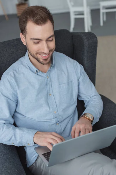 Ritratto dell'uomo sorridente che usa il computer portatile mentre riposa in poltrona — Foto stock