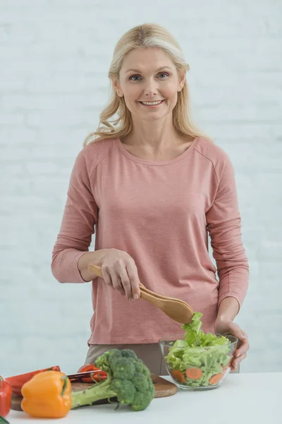 Ritratto di donna matura sorridente che cucina insalata per cena in cucina — Foto stock