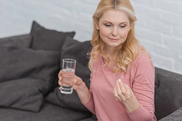 Ritratto di donna matura con bicchiere d'acqua e medicina in mano — Foto stock