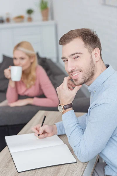 Selective focus of smiling man at table with notebook and mother with cup of coffee at home — Stock Photo