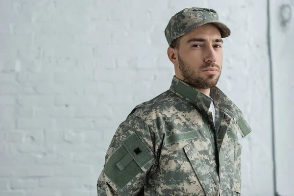 Retrato de soldado em uniforme militar olhando para câmera contra parede de tijolo branco — Fotografia de Stock
