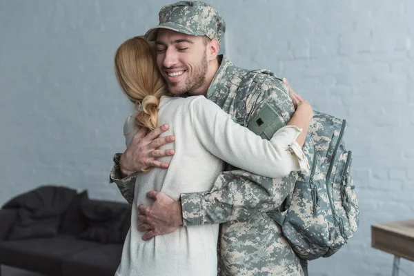 Side view of smiling man in military uniform and mother hugging each other at home — Stock Photo