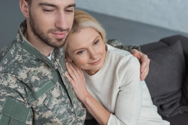 Retrato del hombre en uniforme militar abrazando sonriente madre en casa - foto de stock