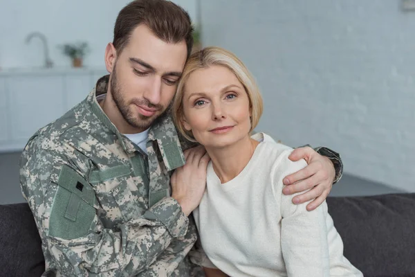 Retrato del hombre en uniforme militar abrazando a la madre en casa - foto de stock