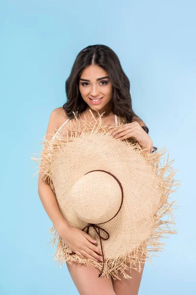 Attractive smiling young woman posing with straw hat, isolated on blue — Stock Photo