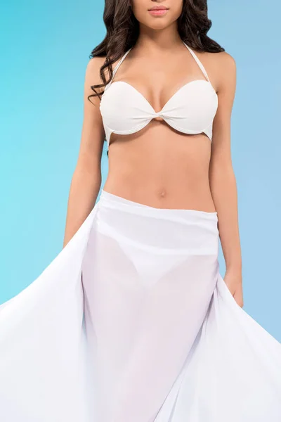 Vista recortada de chica bronceada en bikini blanco posando con velo, aislado en azul - foto de stock