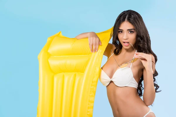 Atractiva chica posando con colchón inflable amarillo, aislado en azul - foto de stock