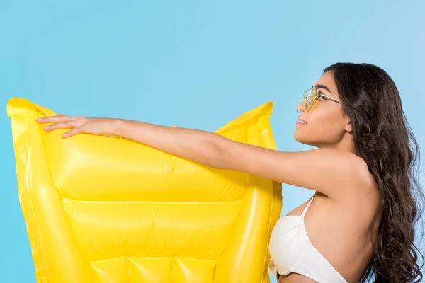 Belle jeune femme en lunettes de soleil jaunes posant avec matelas gonflable jaune, isolé sur bleu — Photo de stock