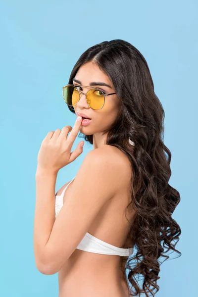 Beautiful brunette girl posing in swimsuit and yellow sunglasses, isolated on blue — Stock Photo