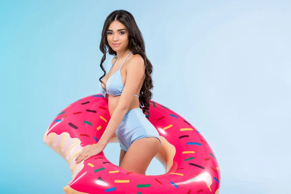 Menina morena atraente posando com anel de donut inflável, isolado em azul — Fotografia de Stock