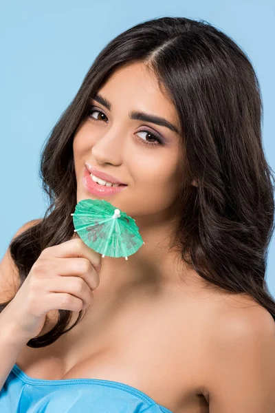 Beautiful young woman holding cocktail umbrella, isolated on blue — Stock Photo