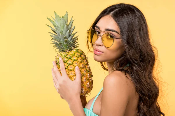 Hermosa chica en gafas de sol sosteniendo piña fresca, aislado en amarillo - foto de stock